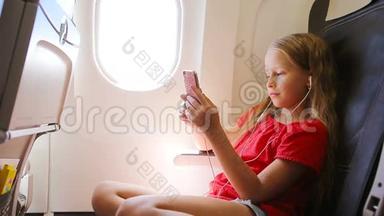 可爱的小女孩坐在靠窗的飞机上。 小孩坐在飞机窗前听音乐